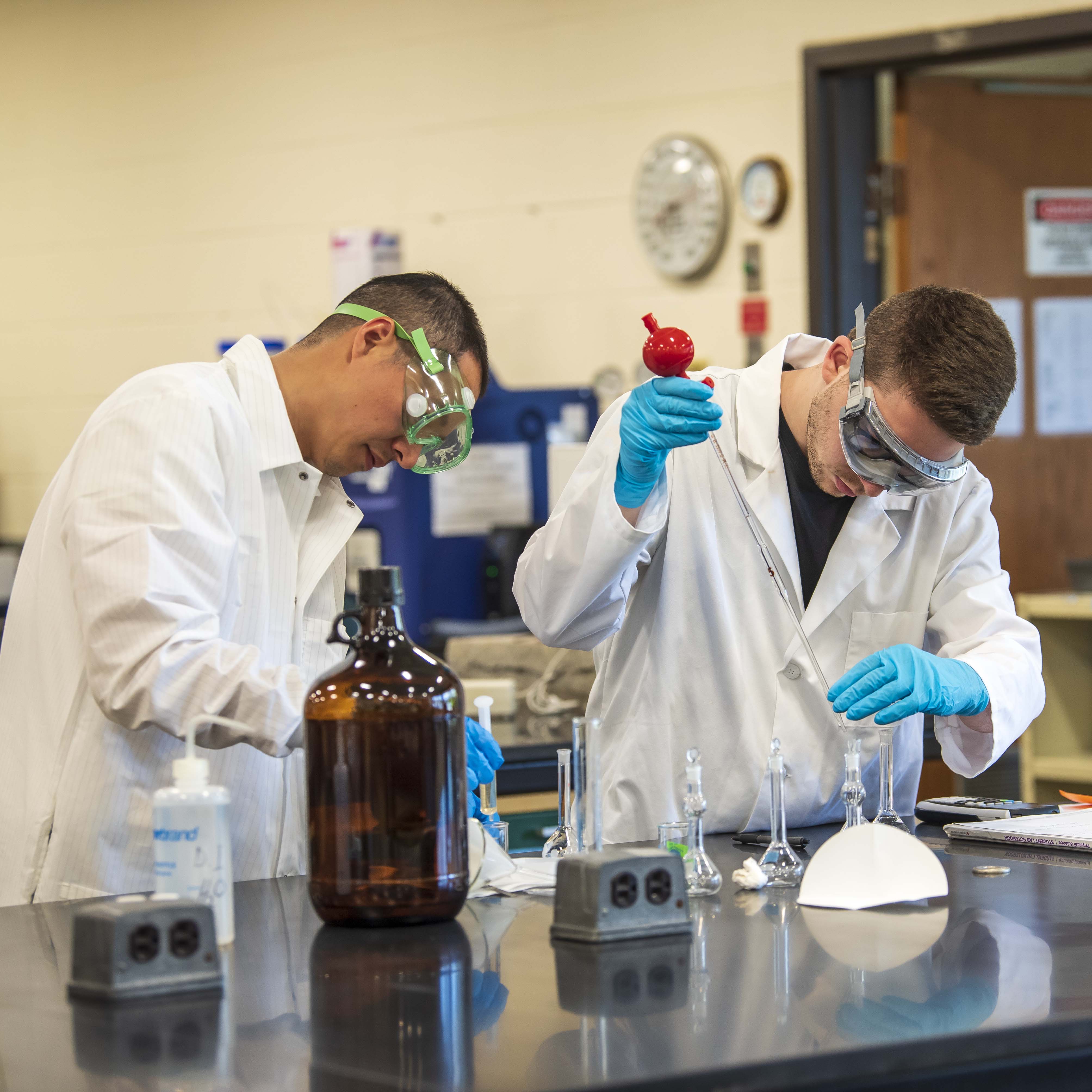 two chemistry students in white lab coats conducting experiments with beakers and liquids
