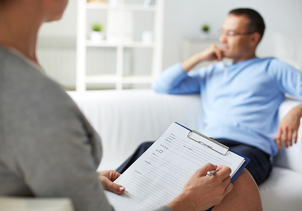 counseling session with a woman taking notes and a man in the distance sitting on a couch