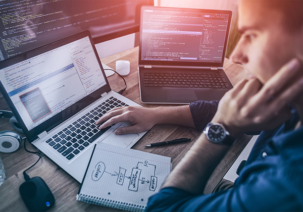 man working on two laptops and a desktop computer on computer coding