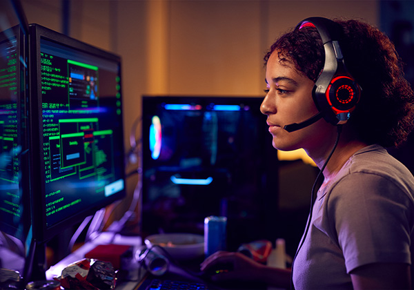 woman with a headset on working on a dual screen computer on coding 