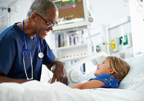 older african american nurse smiling at a young female patient in a hospital bed